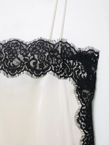 Detailed macro view of delicate black lace trim on a white silk satin camisole top