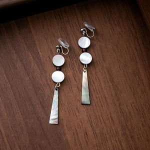 Detail of shell dangle earrings with red beads on dark wood background