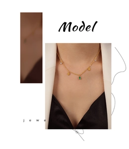 Detail of gold titanium necklace with green rectangular stones and sun pendant on model