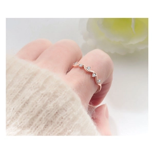 Detail showing wave-patterned rose gold ring with five sparkling zircons on finger