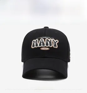 Detailed embroidery of the letters MANY and charm on a black cotton baseball cap