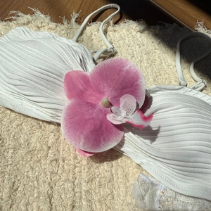 Detailed view of white ribbed bikini top featuring a large pink fabric orchid decoration