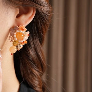 Détail de boucles d'oreilles fleurs avec cristaux orange et perles portées par modèle