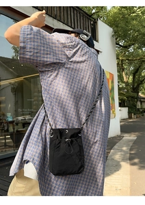 Outdoor street style shot showing a black nylon drawstring crossbody water bottle bag