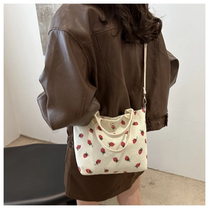 Detail view of white corduroy bucket bag with strawberry embroidery worn as a crossbody