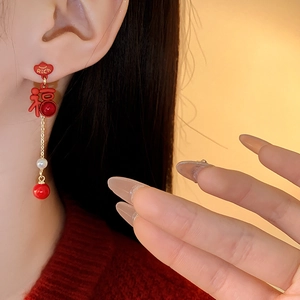 Detail of Chinese style red and gold earrings featuring a pearl and Rich Fu characters