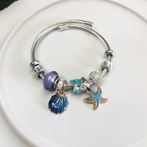 Silver twisted bracelet with blue enamel shell and starfish charms on a white ceramic plate