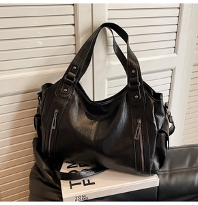 Close-up of black leather tote bag with dual zipper pockets on a stylish leather seat