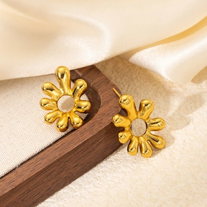 Detailed view of gold-toned titanium steel flower earrings on cream silk fabric texture