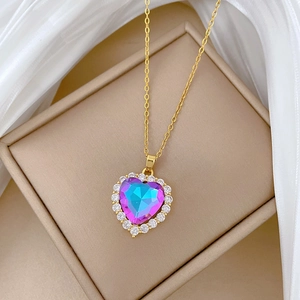 Detail of a golden heart necklace featuring a blue-purple faceted gem and tiny crystals