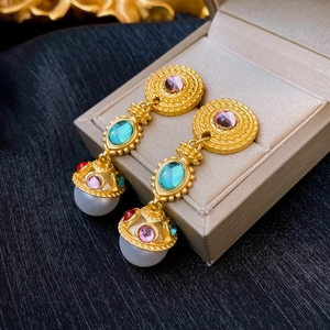 Detailed close-up of vintage gold earrings with colorful gemstones and pearls on a jewelry box
