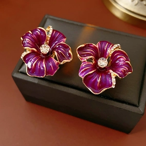 Macro detail of purple enamel flower earrings with gold edges and crystal center