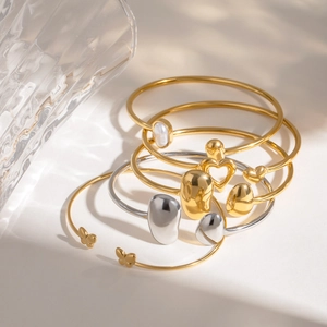 Detail of stacked gold and silver stainless steel bangles with pearl and heart charms