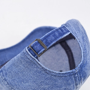 Detail of blue denim baseball cap showing adjustable strap and bronze metal buckle closure