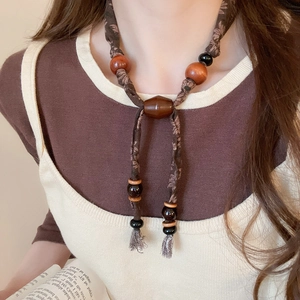 Vue détaillée du collier ethnique en tissu marron, perles en bois et pompons en coton doux