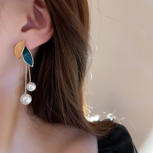 Detail view of leaf drop earrings with white faux pearls and gold chain on a model