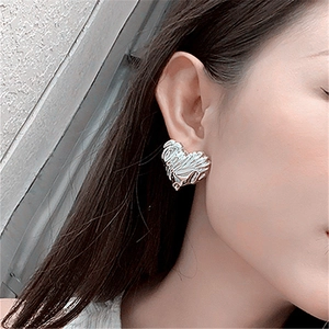 Macro shot of silver heart stud earrings with textured lava pattern on female ear lobe