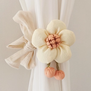 Close-up of beige fabric flower curtain tieback with embroidery and pink pom-poms