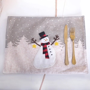 Christmas snowman placemat with embroidered trees and golden cutlery on a table