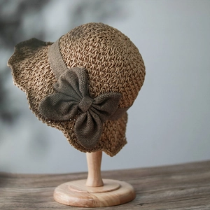 Detail of light brown woven straw hat featuring a dark brown decorative knit bow