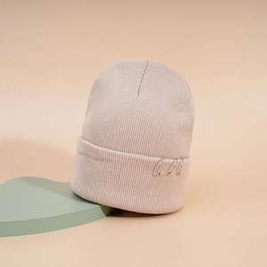 Détail du bonnet en maille beige avec trois anneaux métalliques argentés sur le bord