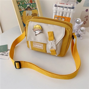 Detail of yellow and beige canvas bag with cute brooch and adjustable strap on a study desk