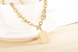 Dettaglio del ciondolo quadrato dorato con chiusura OT su una collana a catena spessa