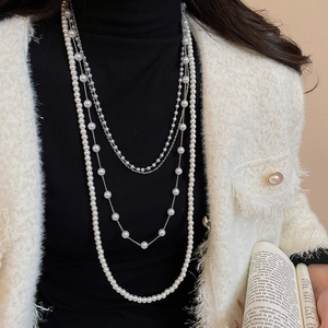 Detail of elegant multilayer pearl necklace with silver chains worn over a chic black outfit