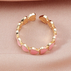 Dettaglio dell'anello aperto in rame dorato con cuori in smalto rosa e misura regolabile