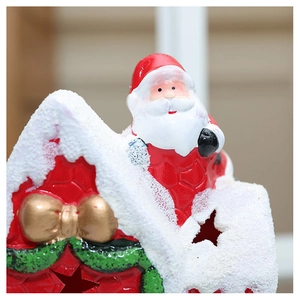 Close-up of ceramic Santa by red snowy house with golden bow and star cutout detail