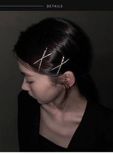 Close-up of dual X-shaped rhinestone hair clips worn on the side of model's hair