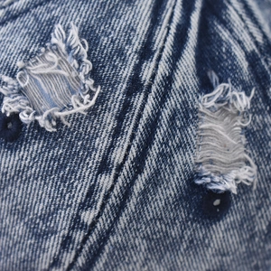 Macro detail of acid wash denim fabric with distressed ripped texture and twill weave