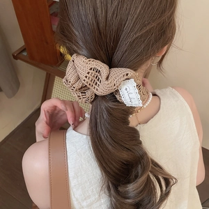 Détail d'un chouchou en crochet beige avec étiquette en dentelle sur une queue de cheval