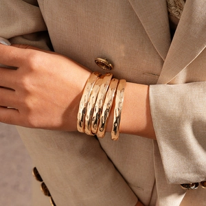 Vue détaillée de cinq bracelets en métal doré martelé portés sur une veste beige chic
