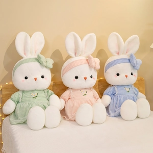 Three plush rabbits in floral plaid dresses with matching bows on a cozy warm bed