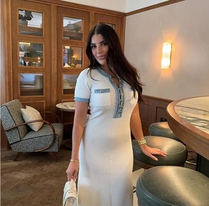 Detail of white knit dress featuring blue denim trim and elegant gold buttons