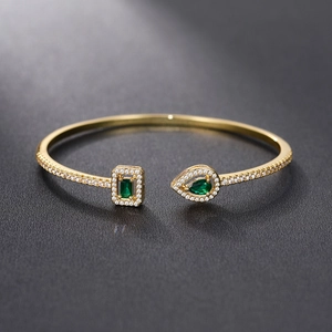 Macro detail of gold cuff bracelet with rectangular and teardrop green zircon stones
