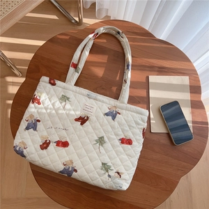 Detailed view of cream quilted tote bag with cute bear and rabbit prints on a wood table