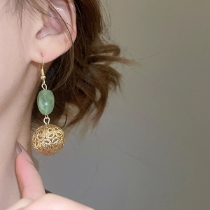 Détail de boucles d'oreilles dorées avec perles en résine verte et pendentifs sphères