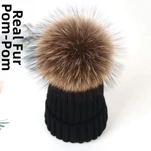 Close-up of black cable knit beanie with large fluffy brown raccoon fur pompom detail