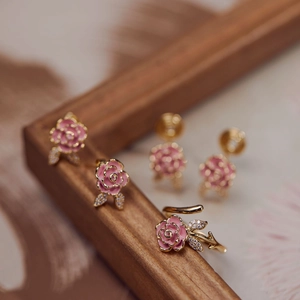 Detailed macro view of pink enamel rose earrings and gold ring set with white zircons