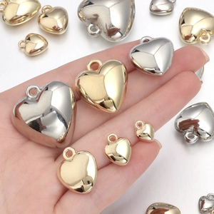 Polished CCB heart pendants in gold and silver colors shown in hand for scale