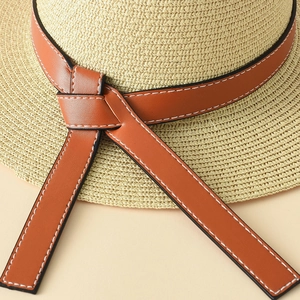 Detail of woven straw fedora featuring a brown leather band with precise white stitching