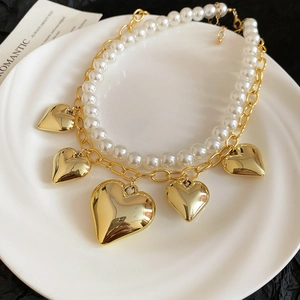 Detail of double layer necklace featuring pearls, gold chunky chains and heart pendants