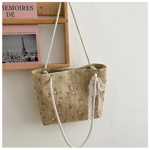 Detail of straw tote bag featuring delicate floral embroidery and white lace decoration