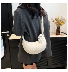 Detail of white quilted crescent bag with plush bunny pendant on wide padded shoulder strap