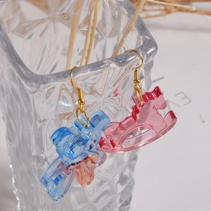 Pink and blue resin rocking horse drop earrings hanging on a clear glass vase