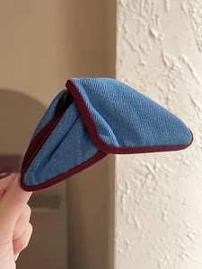 Detail view of denim fabric triangular hair clip with red piping and unique folding structure