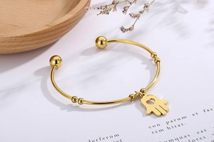Macro detail of gold-plated Hamsa hand charm and heart cutout on open cuff bracelet