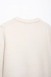 Detail view of white soft knit cardigan featuring raglan sleeves and ribbed round neck